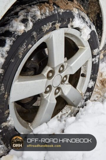 Close-up of an SUV front tire and alloy wheel packed with snow on a snowy mountain road