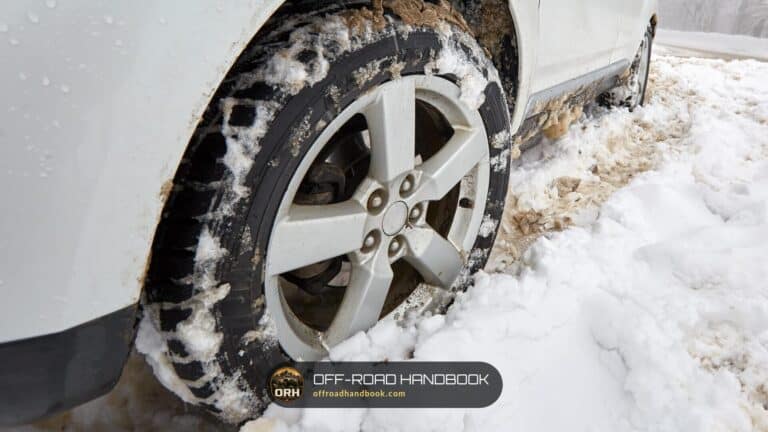 Close-up of an SUV front tire and alloy wheel packed with snow on a snowy mountain road