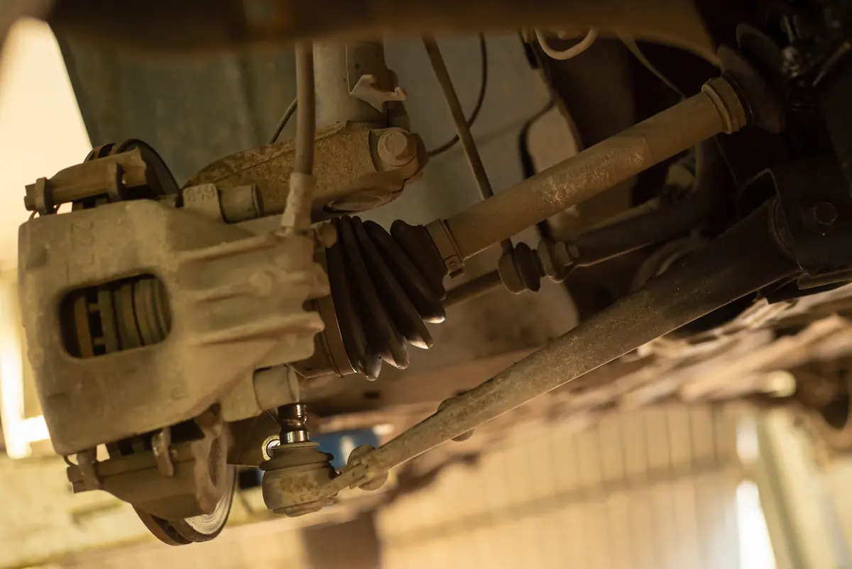 Underside of a vehicle on a service lift showing the driveshaft, CV boot and suspension parts