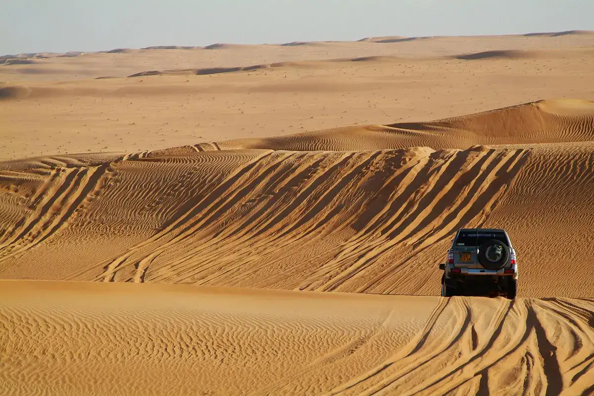 SUV driving on a sand dune with tire tracks across the slope