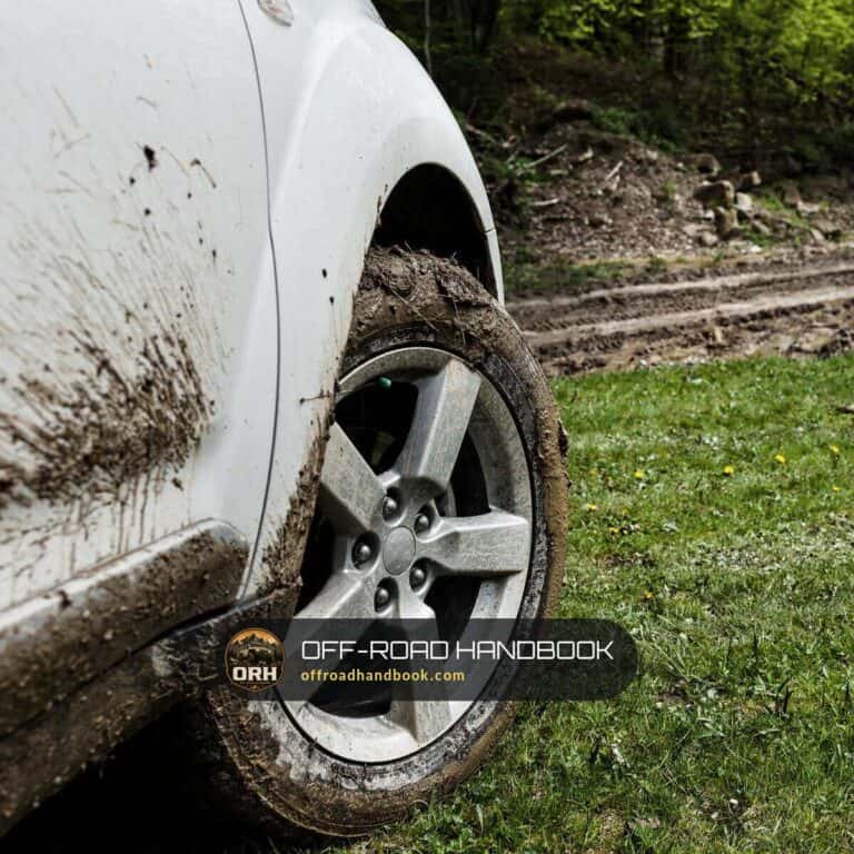 Mud-caked front wheel of a white 4x4 SUV beside a muddy dirt track — Off-Road Handbook