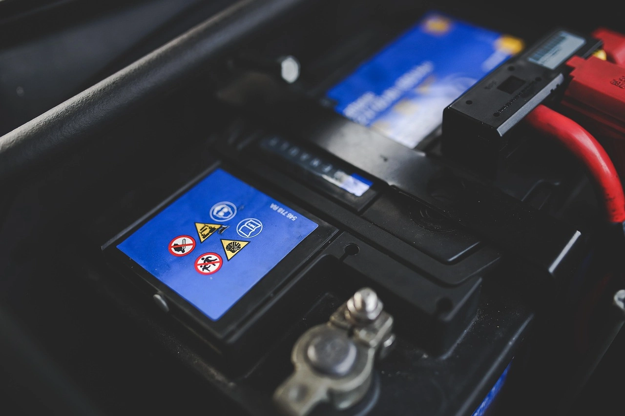 Top of a 12-volt battery with a blue warning label and a terminal under the hood