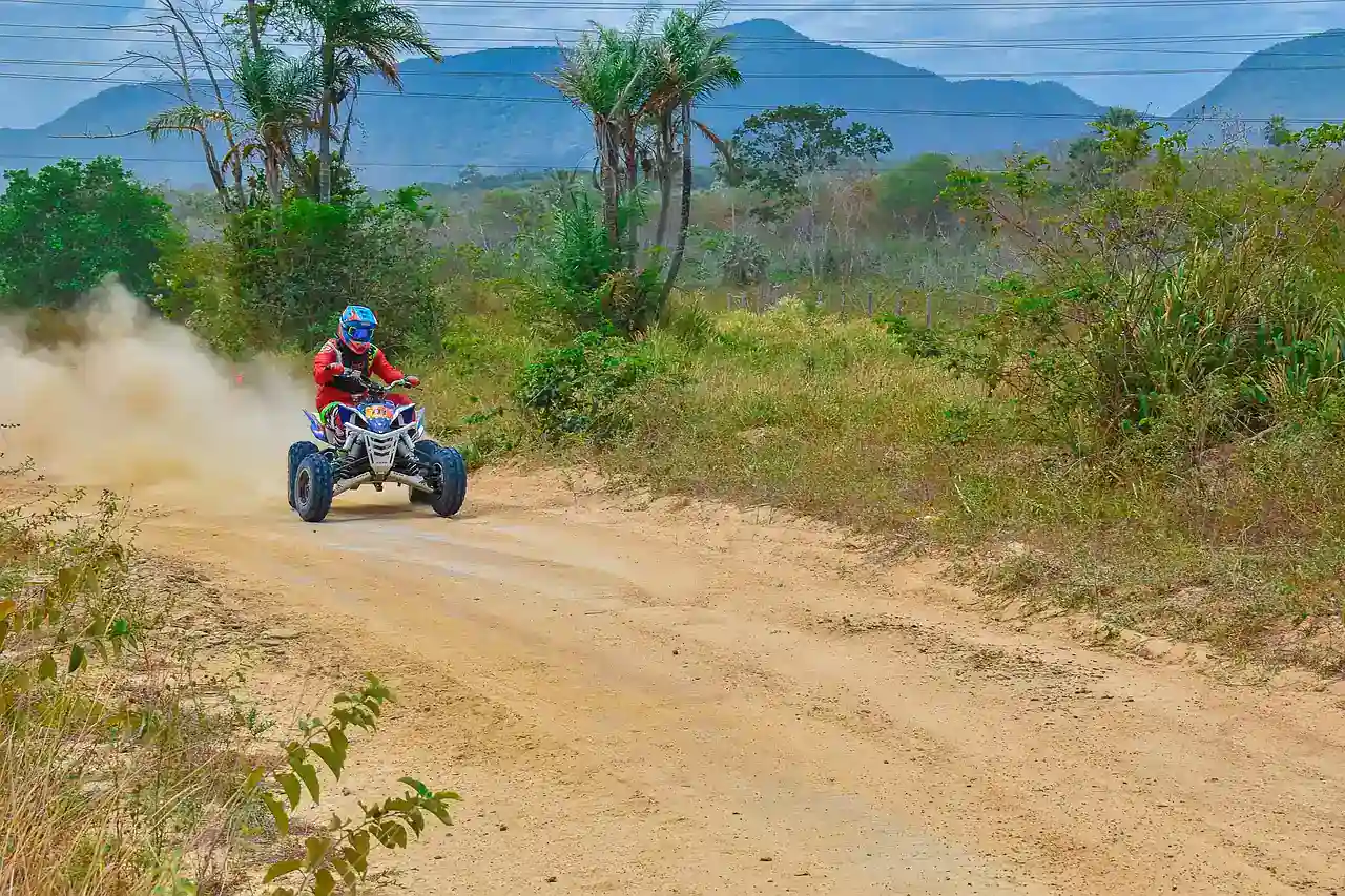 Rider on a quad bike kicking up dust on a dirt road with hills behind