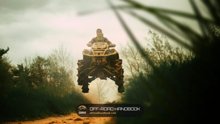 Rider on a four-wheel ATV airborne on a dirt trail between brush