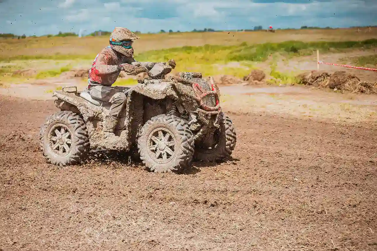 Rider on a mud-covered ATV turning on a muddy dirt track