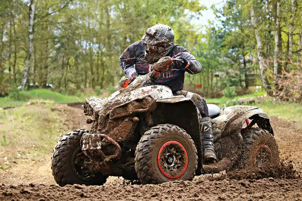 Rider on an ATV caked in mud on a dirt track
