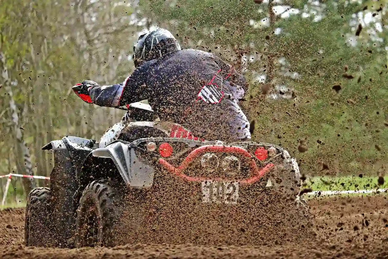 Rider on an ATV throwing mud from the rear wheels on a muddy track