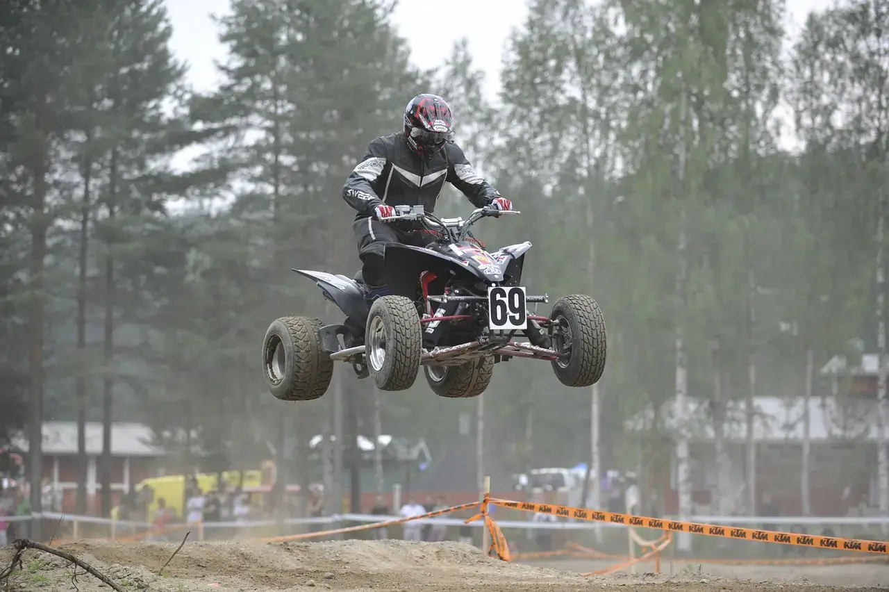 ATV rider in a helmet, goggles and armored black jacket with the quad airborne at a track event