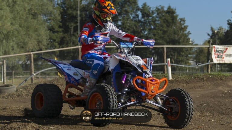 ATV rider in a full-face helmet, goggles, gloves, jersey and pants riding a quad on a dirt track