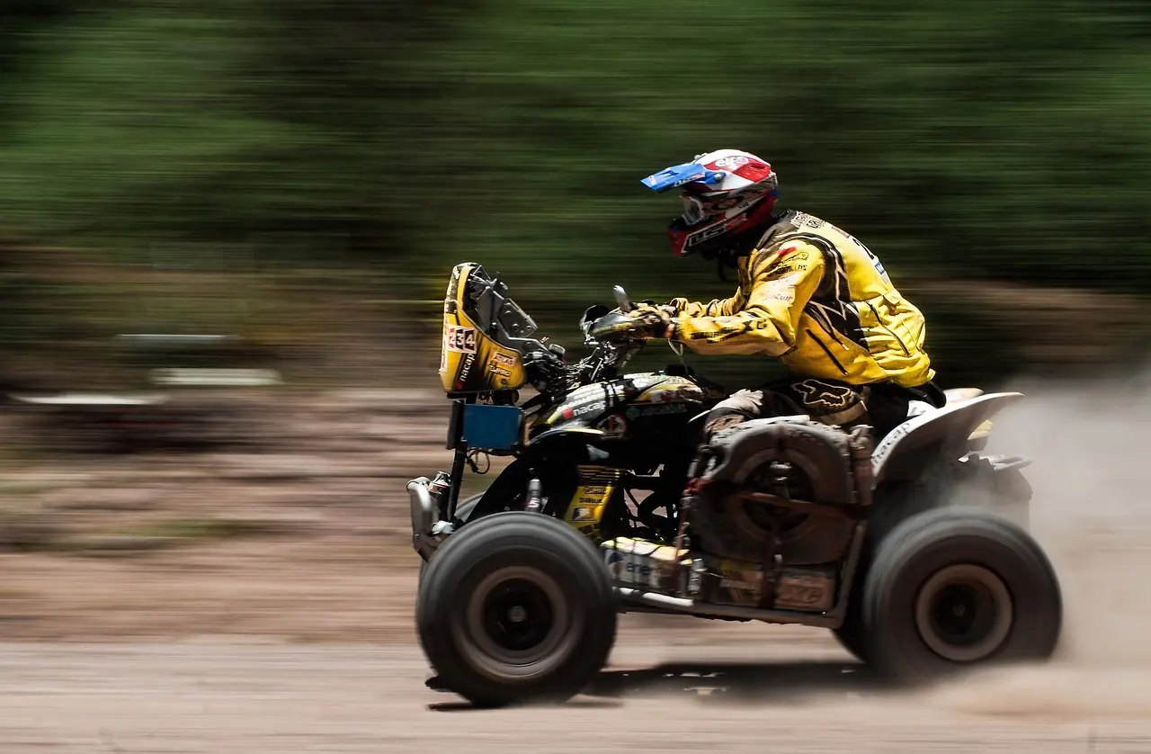 ATV rider in a full-face helmet and padded yellow riding jacket on a quad kicking up dust
