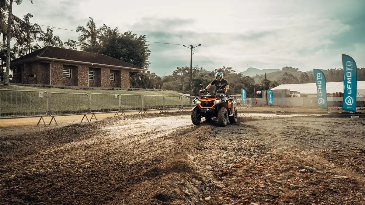 A rider on a quad ATV turning on a wet, muddy dirt track