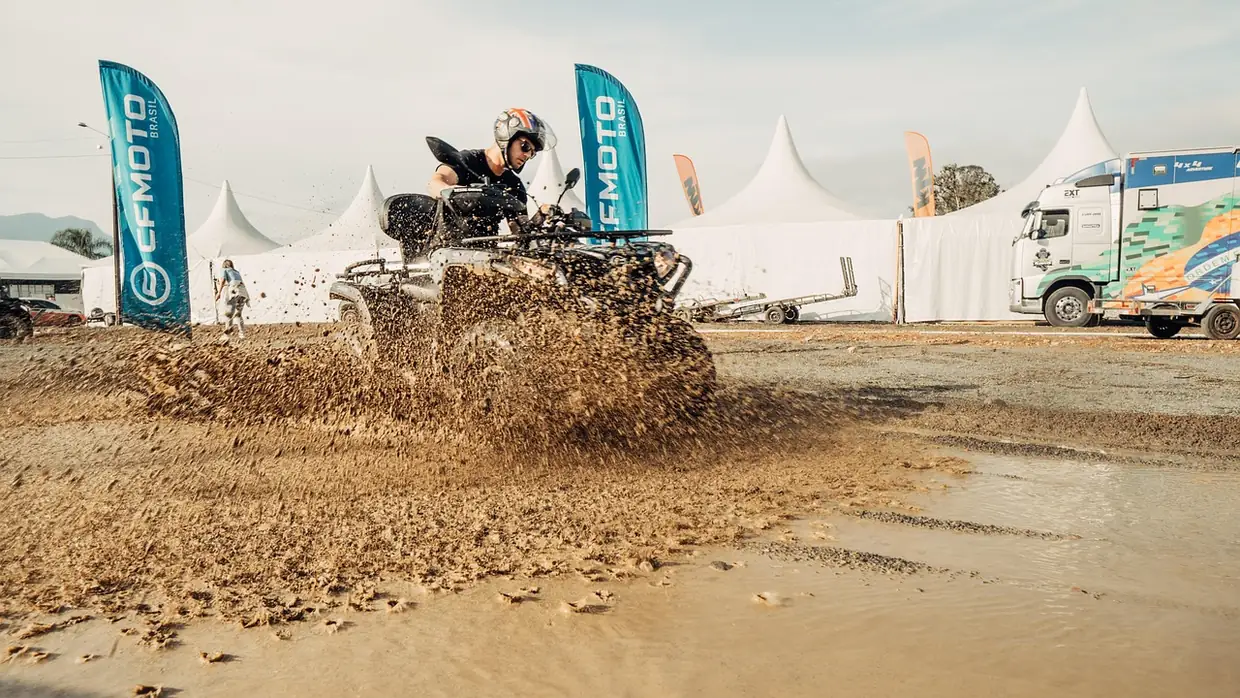 Rider on an ATV throwing mud while crossing a wet dirt course at an event