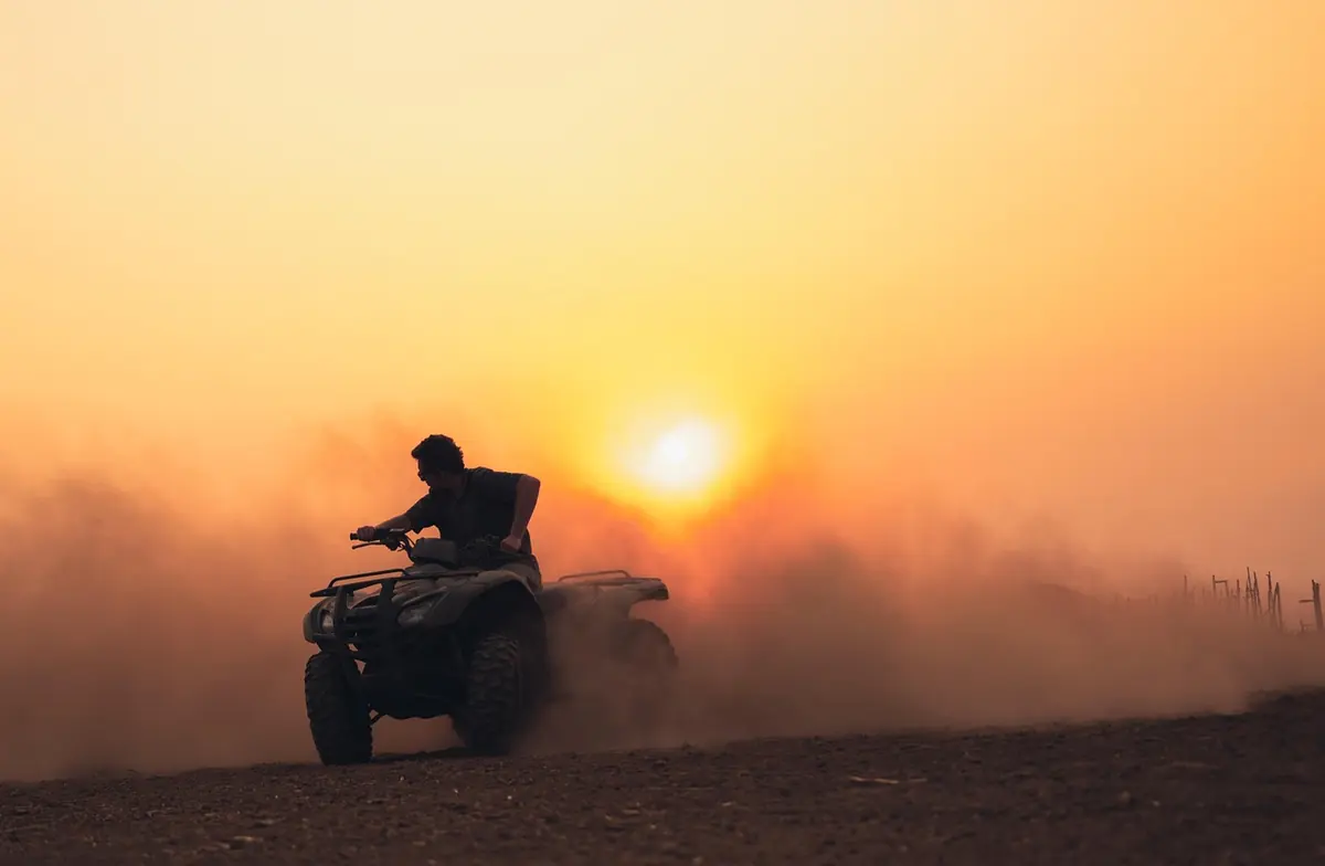 Silhouette of a rider on an ATV kicking up dust at sunset