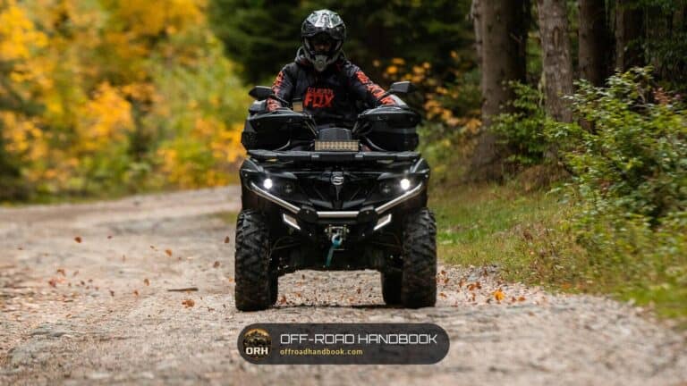 Rider on a black ATV facing the camera on a gravel forest road