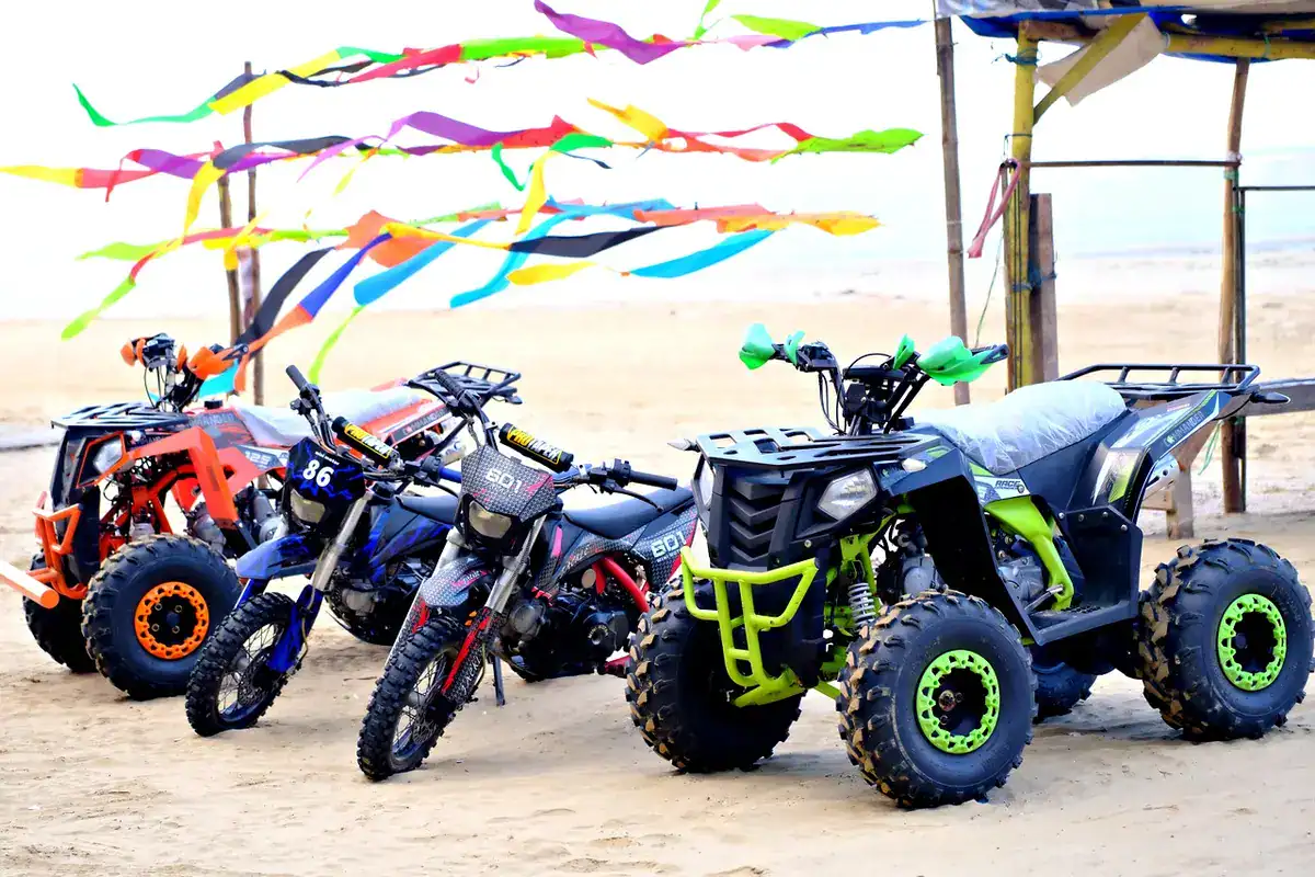 Row of small youth-size ATVs and dirt bikes parked on a sandy beach under colorful ribbons