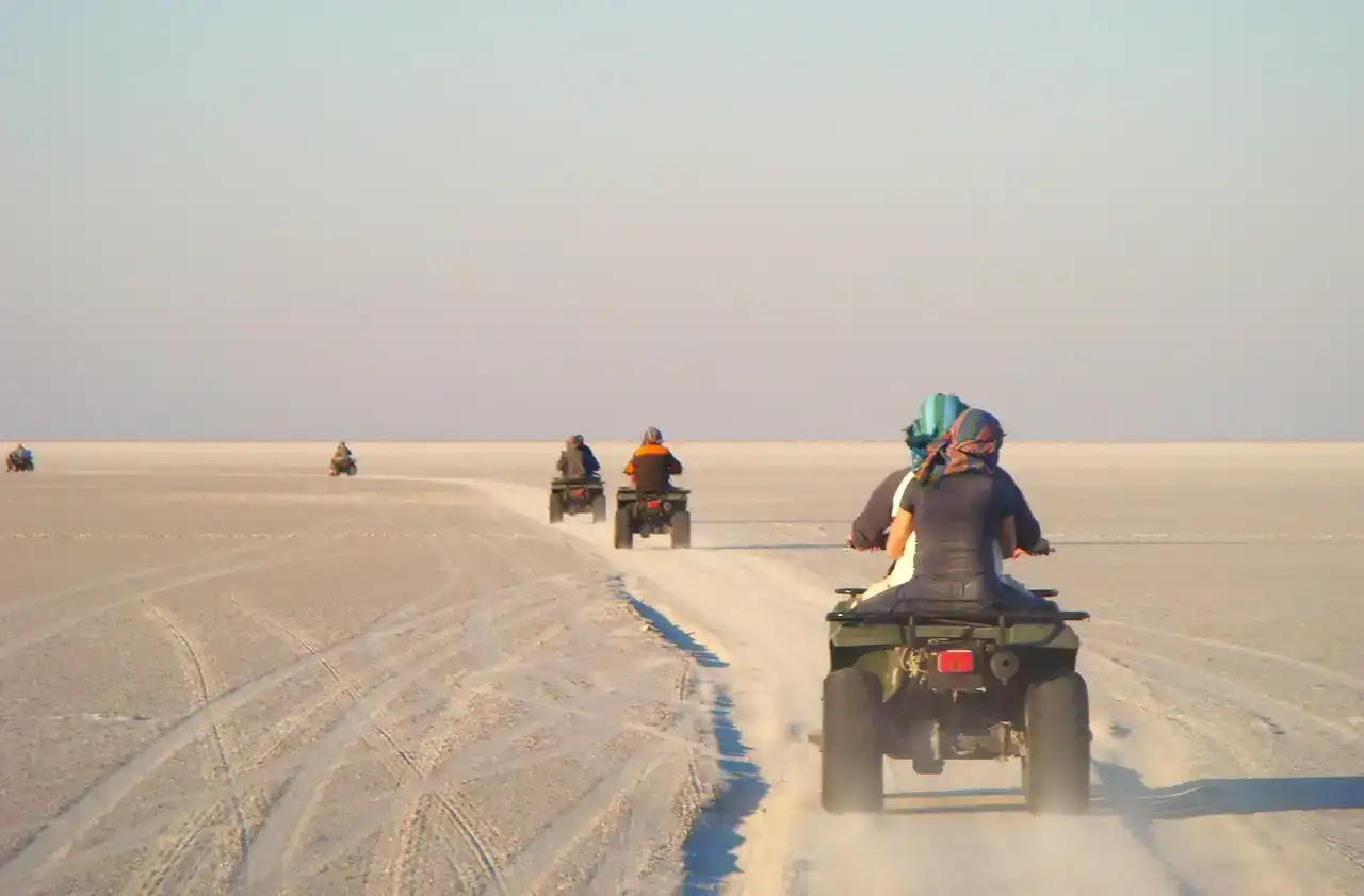 Riders on ATVs crossing a flat, pale stretch of sand
