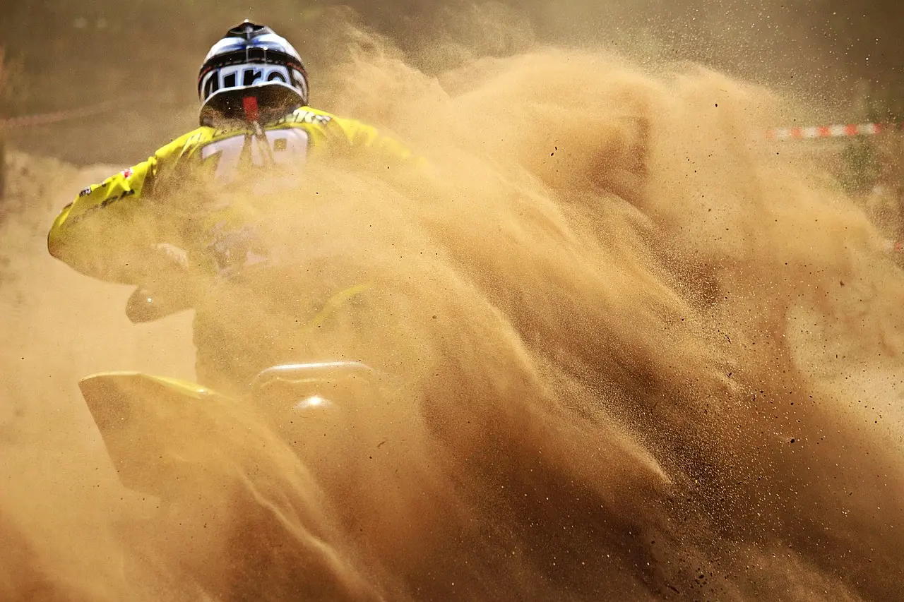 ATV rider in a yellow jersey wrapped in a cloud of dust on a sandy track