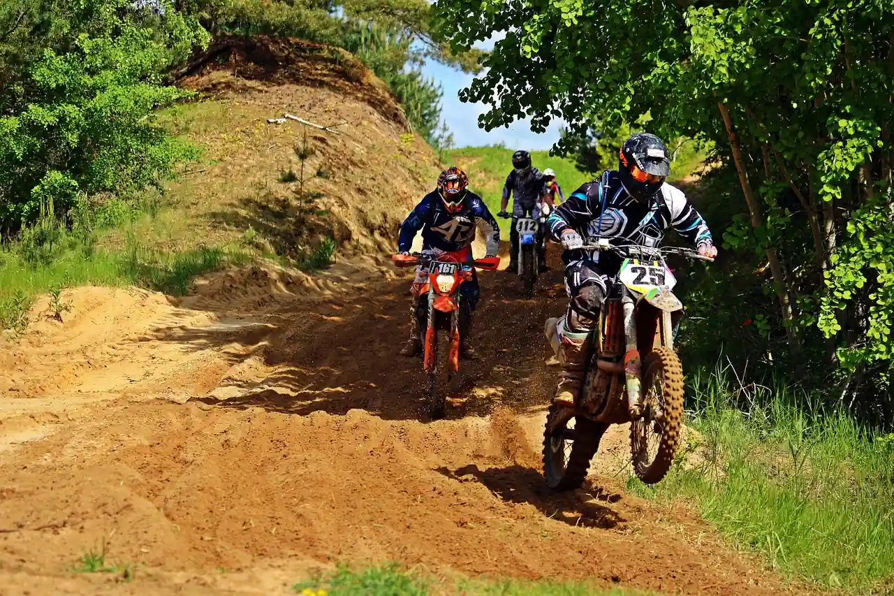 Several dirt bike riders coming down a sandy forest trail between hills and trees