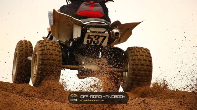 Rear view of a sport quad ATV throwing dirt as it leaves a dirt berm