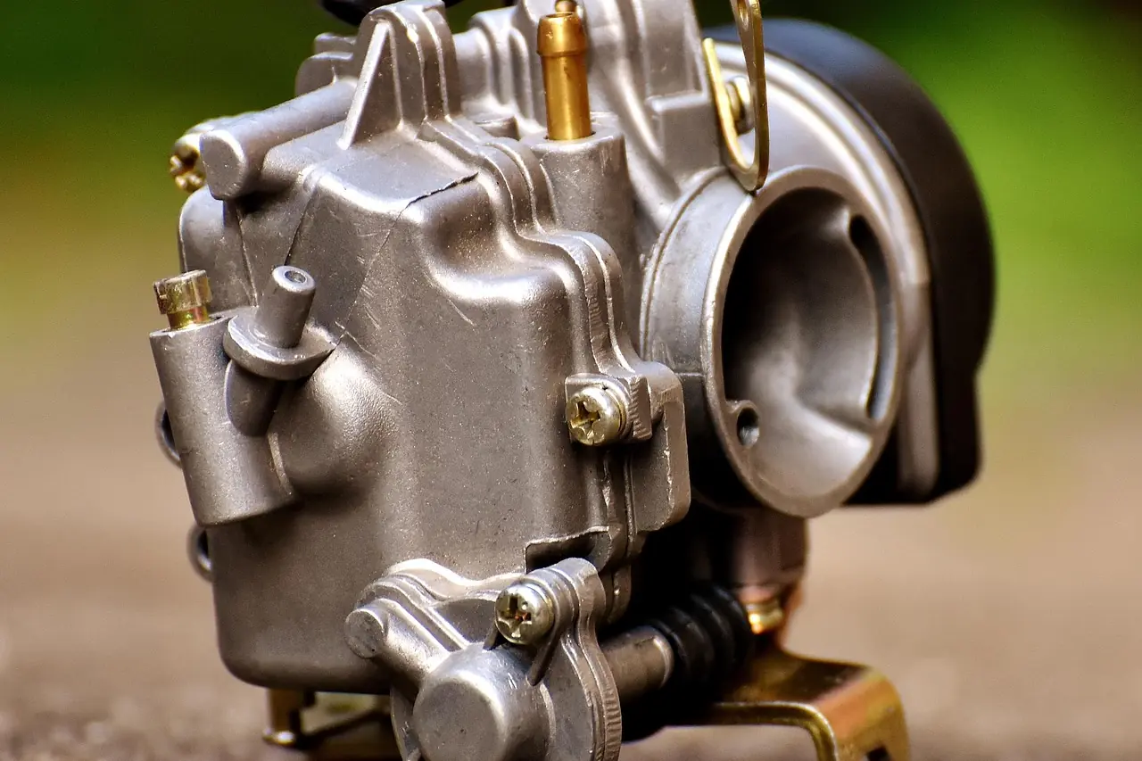 Close-up of a small motorcycle carburetor with its float bowl, throttle slide housing and brass jets (generic carburetor, not a Keihin CVK)