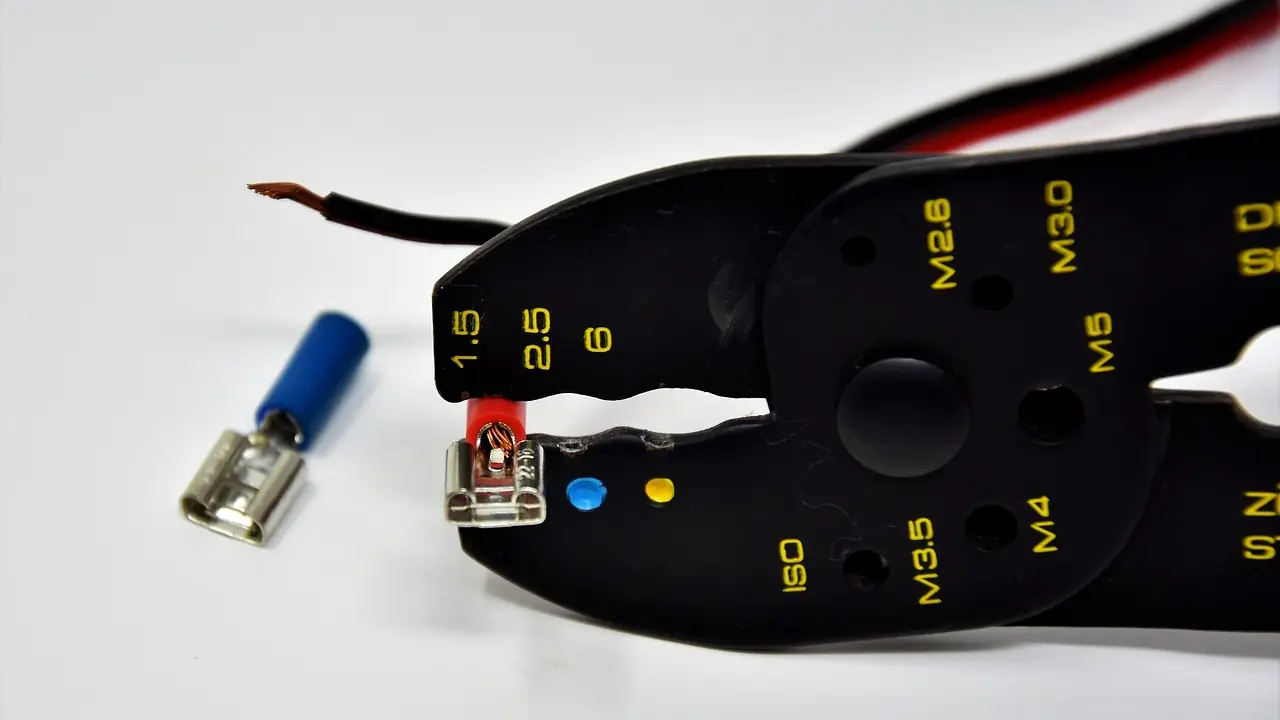 Crimping pliers beside a blue insulated spade terminal on a wire, the repair used for corroded or loose electrical connectors