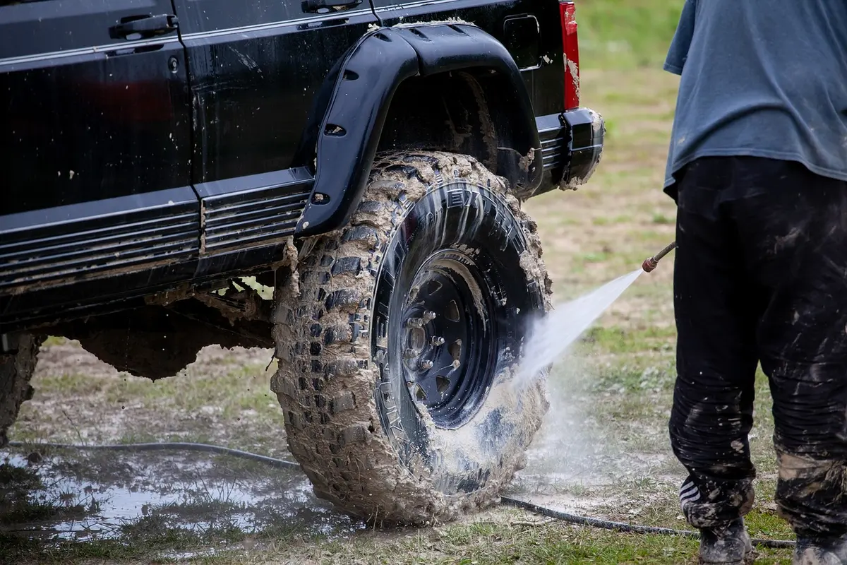 Large mud-terrain tire on a lifted black 4x4 being rinsed after a muddy trail