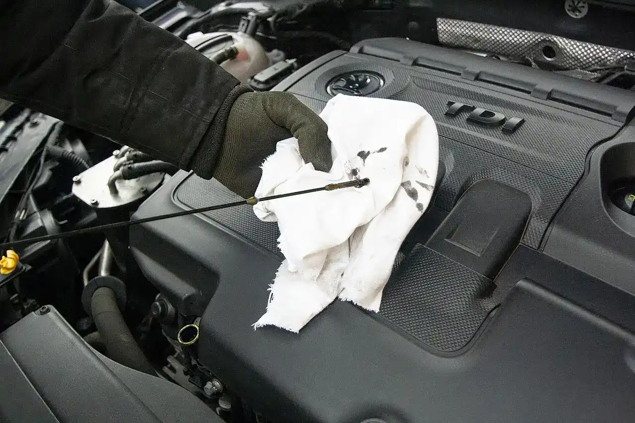 Gloved hand wiping an engine oil dipstick clean on a white rag before reading the level