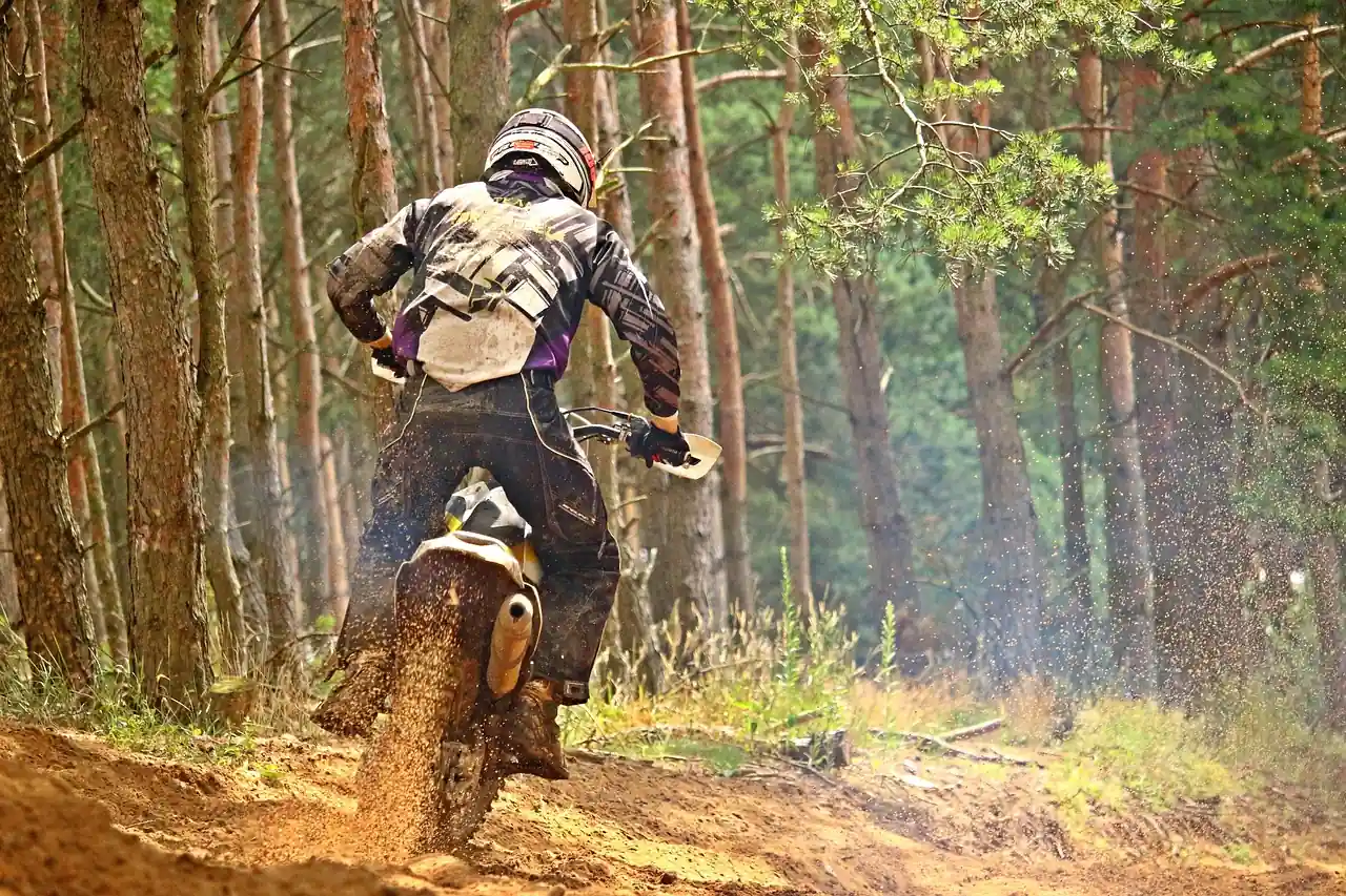 Dirt bike rider in full gear leaning through a sandy forest trail