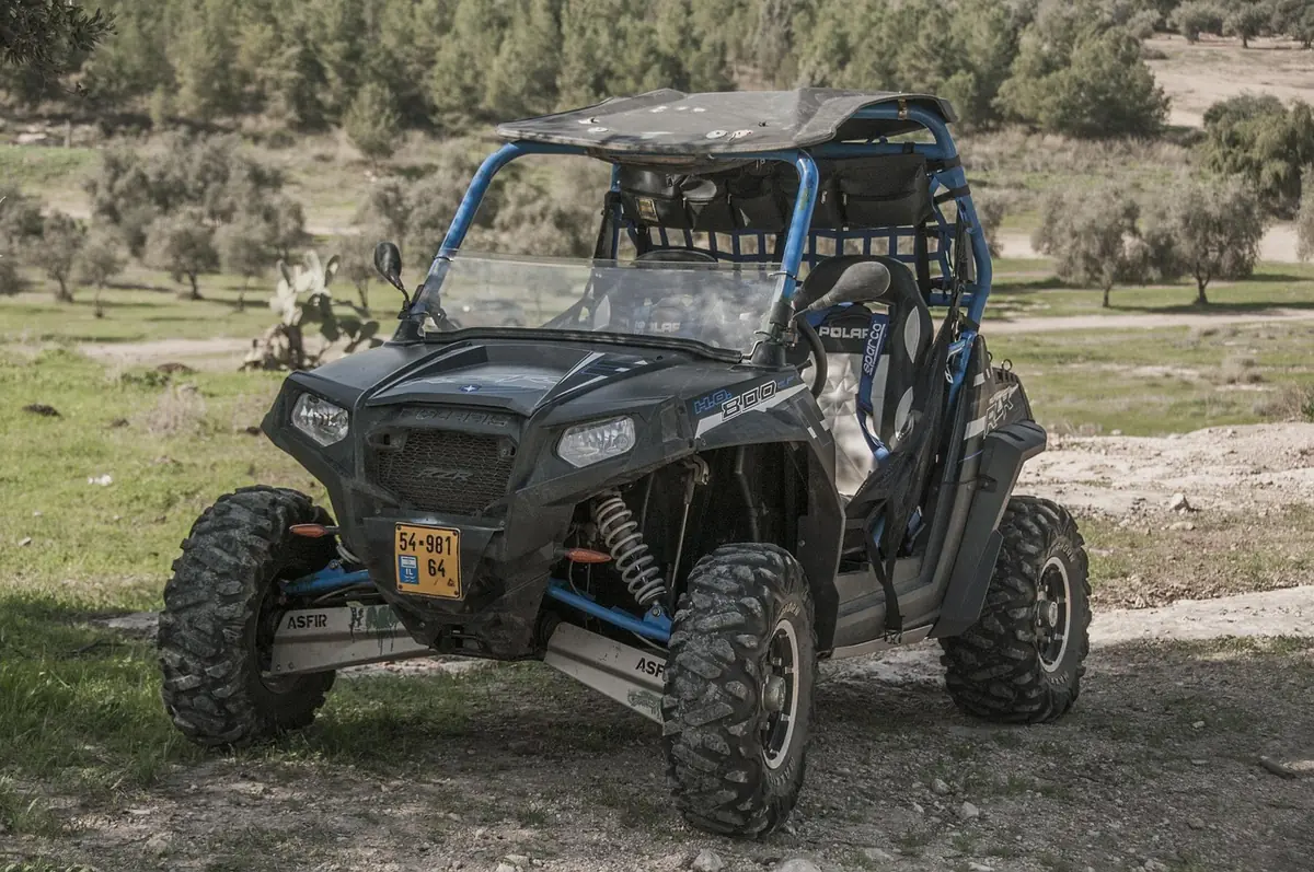 Black side-by-side UTV with roll cage and blue trim parked on a dirt trail, front view