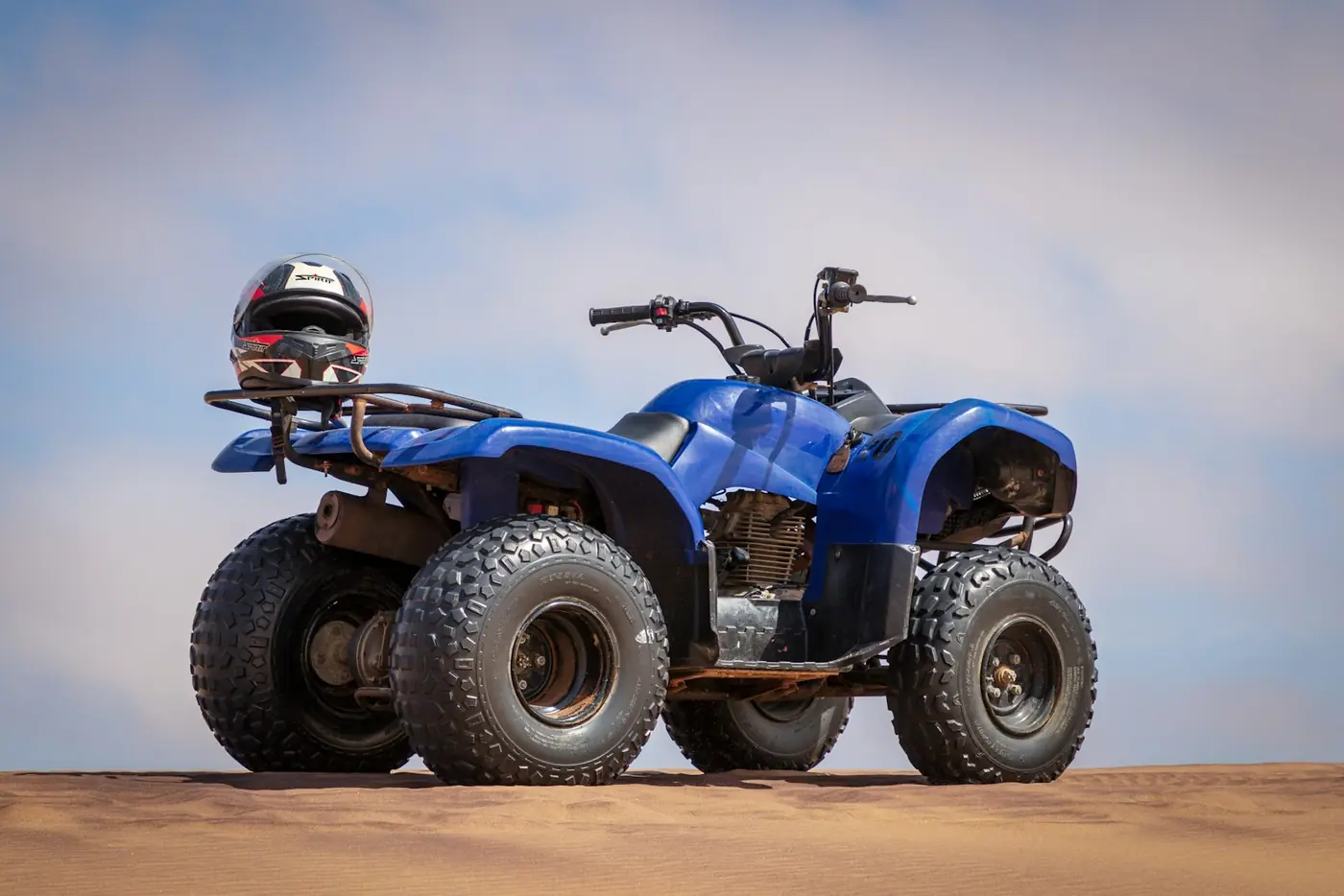 Blue utility ATV on sand with a helmet resting on the rear rack