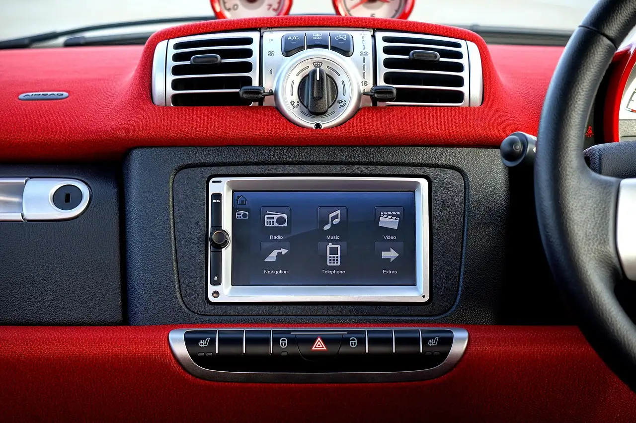 Red car dashboard with a small touchscreen radio above a row of buttons