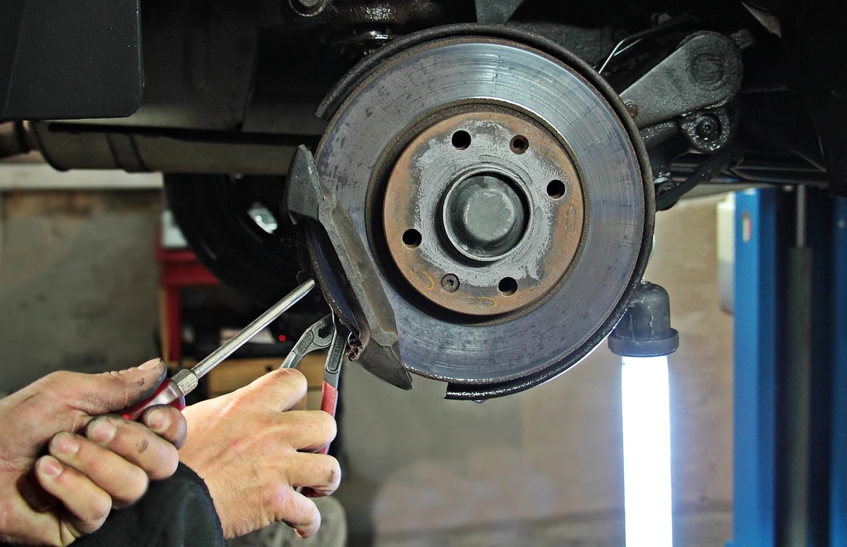 Hands using a screwdriver and pliers at a brake rotor and hub on a car in a garage