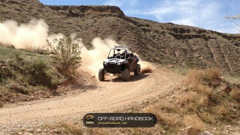 Side-by-side UTV kicking up a dust cloud on a dirt trail in a desert canyon near St. George, Utah