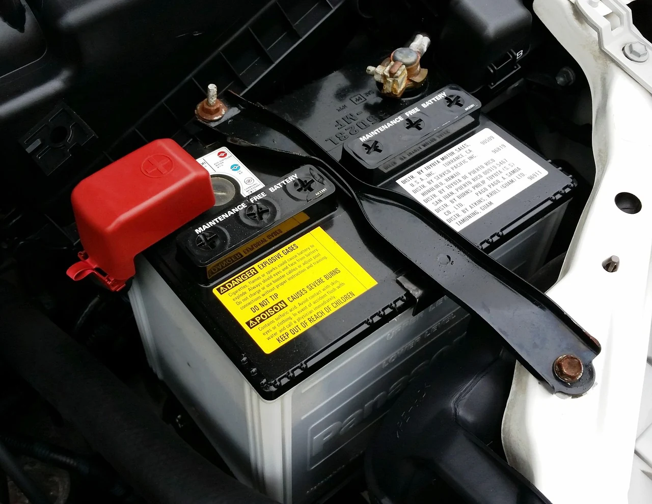 Car battery under the hood with a red cover over the positive terminal