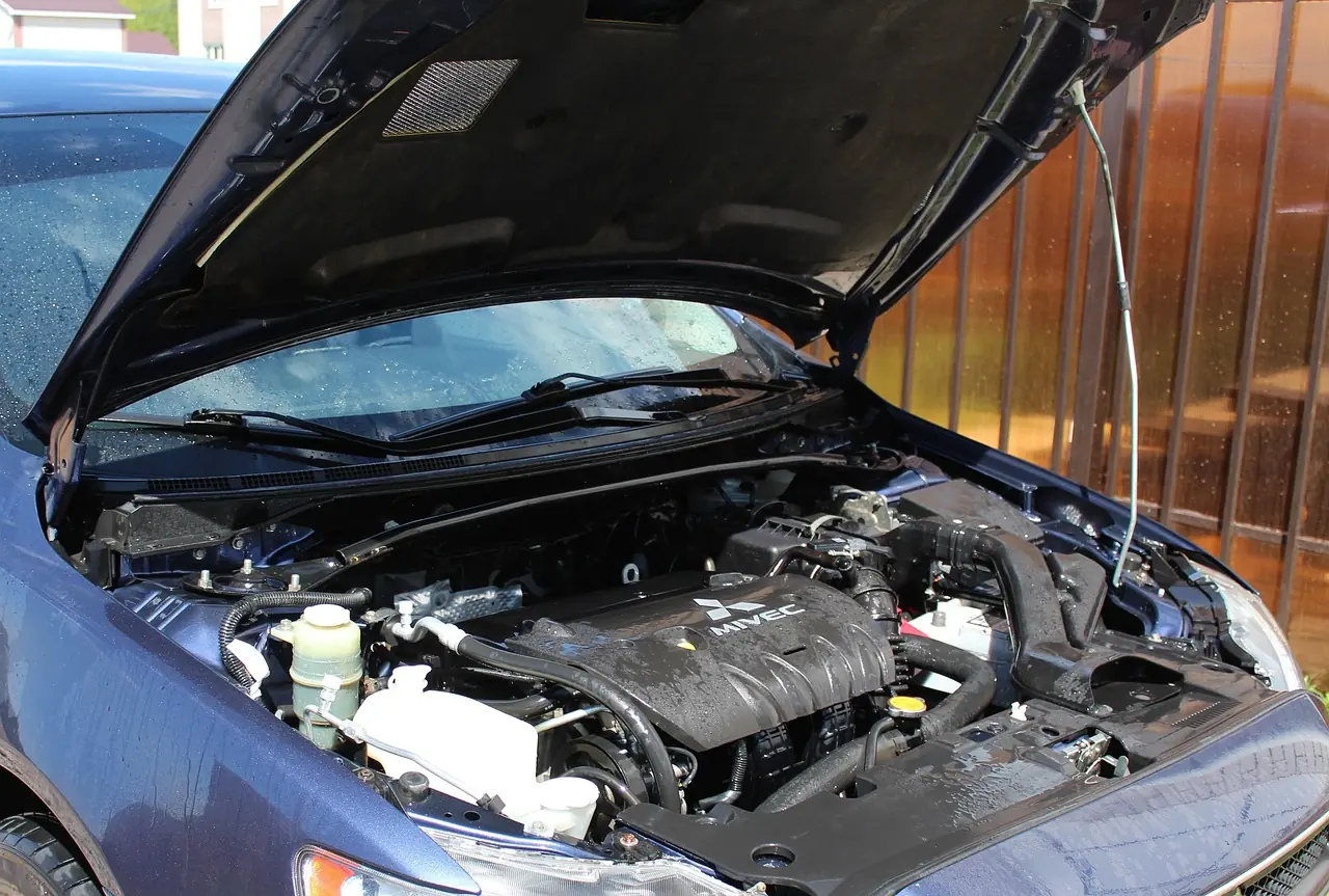 Engine bay of a passenger car with the hood raised, showing the engine, hoses and a plastic fluid reservoir