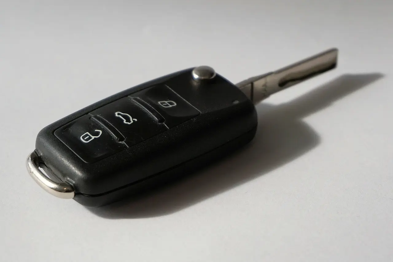 Black car key fob with lock and unlock buttons and a folding metal key on a light surface
