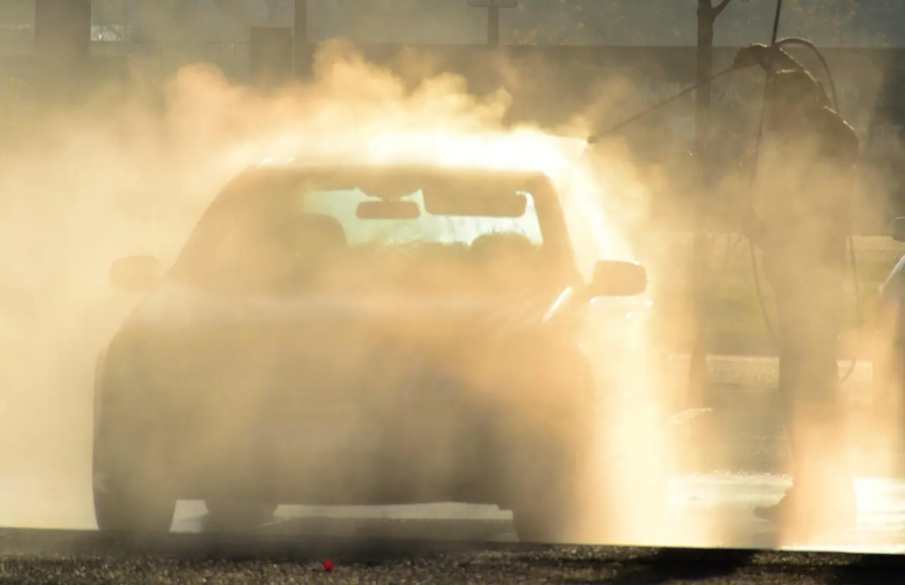 Car at the entrance of an automatic car wash surrounded by a cloud of spray and backlit mist