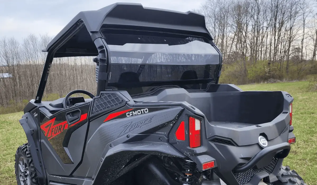 Rear of a dark CFMOTO ZFORCE side-by-side with cargo box, roll cage and roof on a grass field