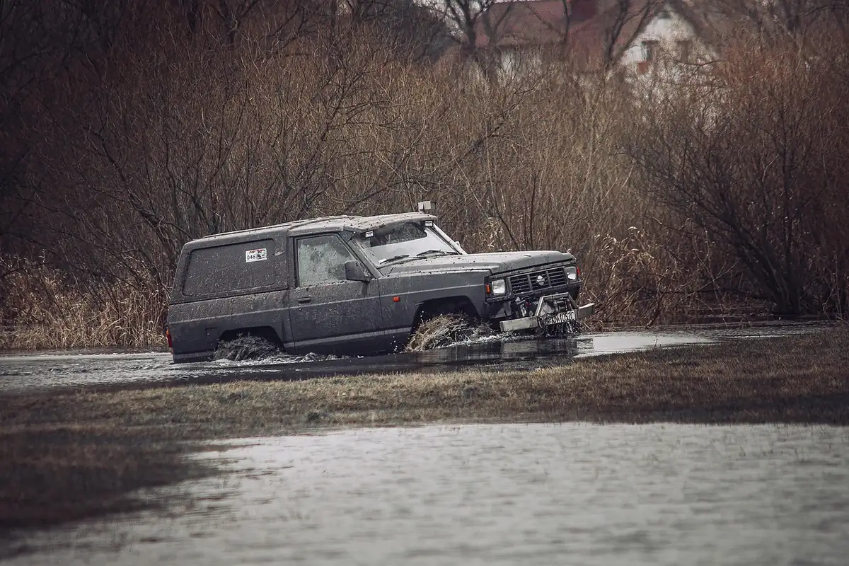 Dark 4x4 wagon driving through a muddy water crossing