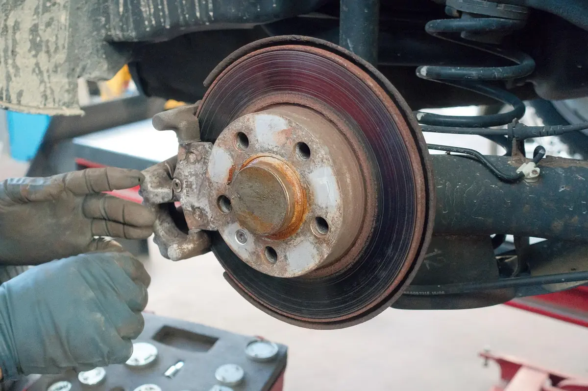 Gloved hands on a brake rotor beside a coil spring under a car
