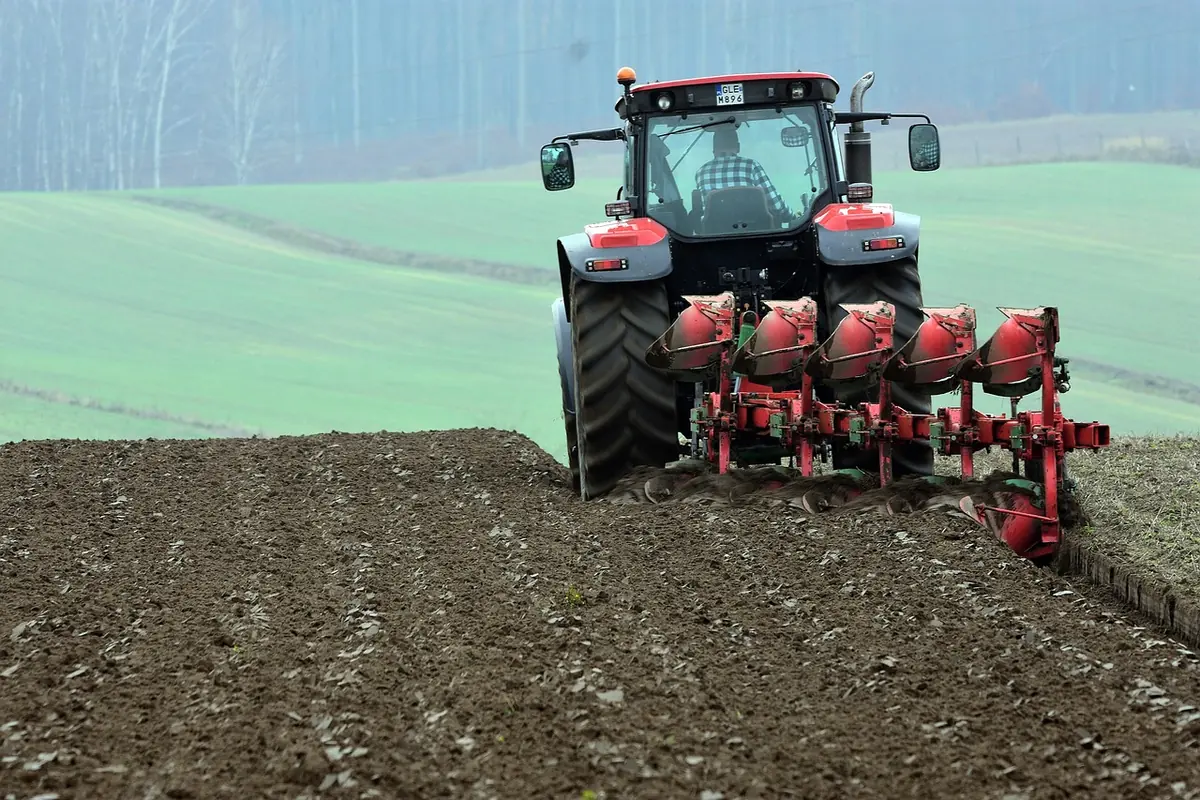 Red tractor pulling a plow across dark soil on a farm field