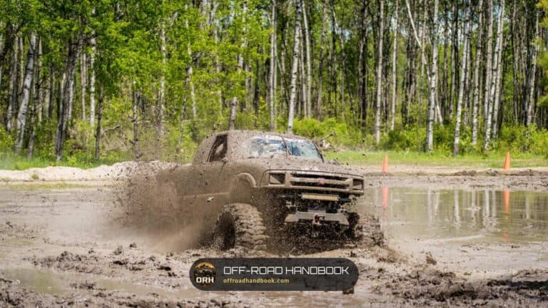Lifted pickup truck plowing through a deep mud pit with mud spraying off the tires