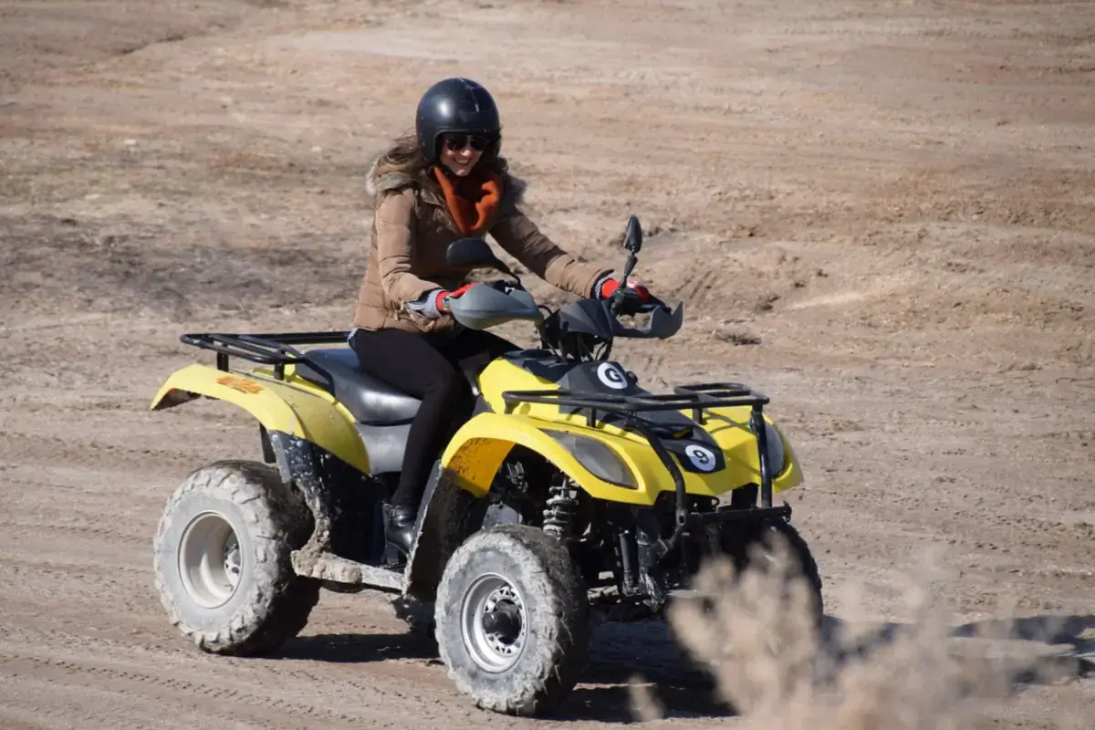 Helmeted rider on a yellow ATV riding on a dry dirt trail