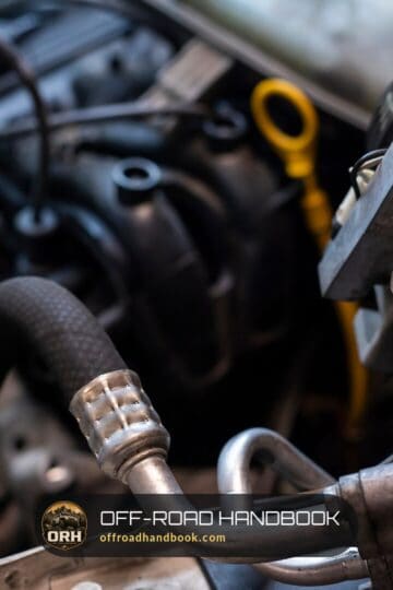 Close-up of a car engine bay with hoses and the yellow oil dipstick handle — Off-Road Handbook
