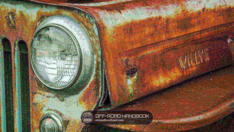 Rusty fender of an old Willys Jeep with a round headlight, grille slots on the left and the Willys name stamped in the metal
