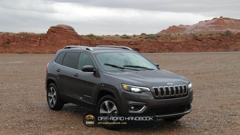 Gray Jeep Cherokee SUV parked on gravel in front of red rock formations