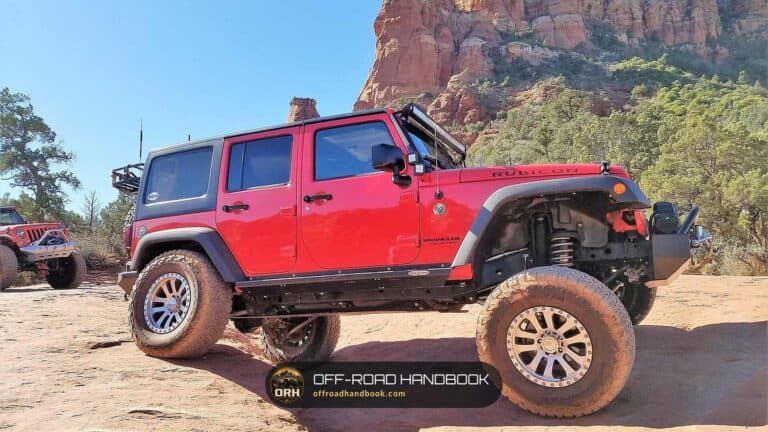 Red four-door Jeep Wrangler Rubicon parked on red sandstone with a rock butte behind it