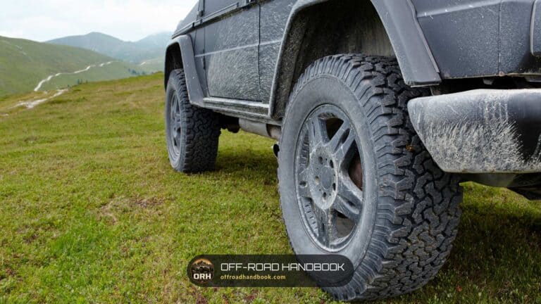Lifted gray 4x4 SUV with mud on its all-terrain tires parked on a grassy mountain meadow — Off-Road Handbook