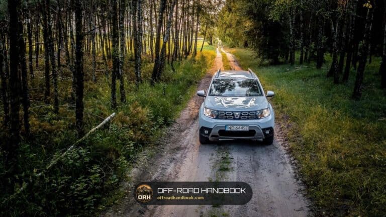 Compact crossover SUV driving toward the camera on a sandy forest dirt road lined with trees; not a Ford Edge