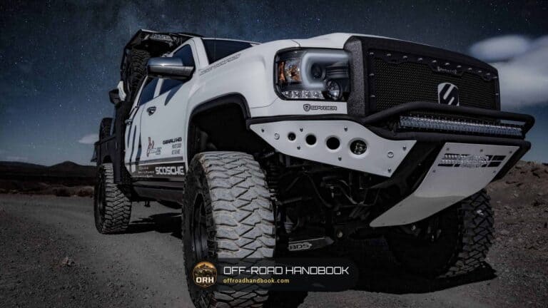 Lifted white pickup truck with large mud-terrain tires parked on a gravel road under a night sky